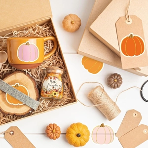 Flat lay of an autumn gift set with a pink pumpkin mug and decorative stickers in a kraft box
