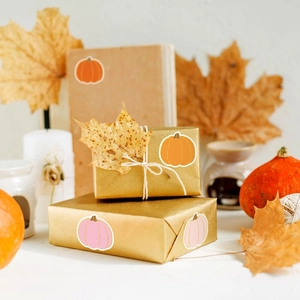 Close-up of decorative pumpkin stickers on a gift box with autumn maple leaves and candles
