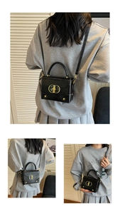 Détail d'un sac bandoulière noir effet froissé brillant avec boucle dorée en forme de D