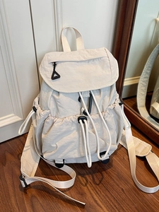 Minimalist beige nylon drawstring backpack with flap closure on wooden floor