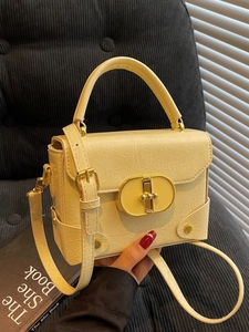Sac à main bandoulière jaune pâle en cuir texturé avec fermoir doré sur un fauteuil
