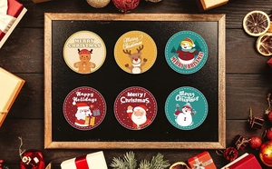 Close-up of circular Christmas stickers featuring snowman and reindeer on wooden background