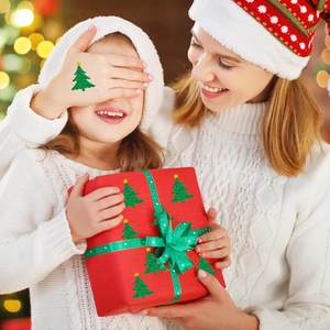 Primer plano de pegatinas de árboles de Navidad verdes brillantes en mano y caja de regalo
