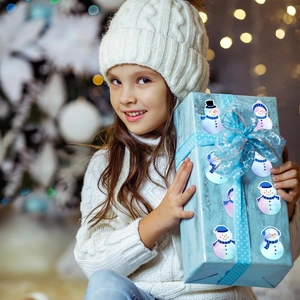 Detail of laser snowman stickers on a blue gift box held by a girl near a Christmas tree