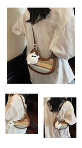 Detail of a woven crescent bag with rainbow stripes and a plush monster charm pendant