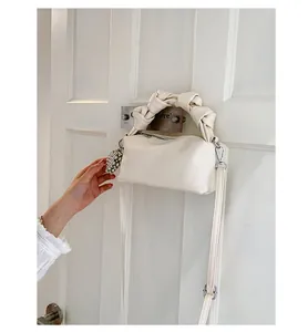 Detail of white pleated handbag with knotted handle and pearl charm hanging on door