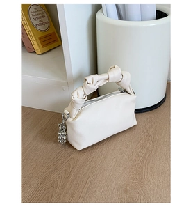 Detail of minimalist cream square handbag with knotted handle and silver bead charm