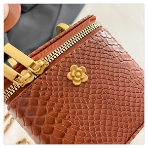 Macro shot of brown faux crocodile skin texture and gold camellia flower detail on a mini bag