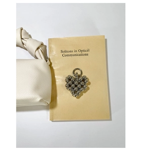 Detailed view of a silver beaded heart charm on a white knotted leather cloud bag