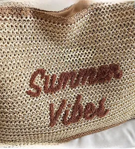 Close-up of embroidered Summer Vibes letters on a beige woven straw tote bag surface