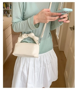 Close-up of cream textured leather square bag with unique knotted handle and strap