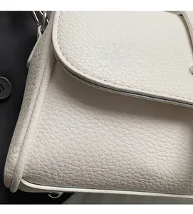 Close-up of white pebble grain leather texture and metallic side hook on the crossbody bag