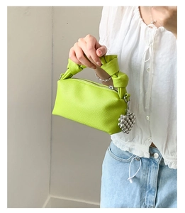 Detail view of neon green pleated handbag featuring knotted handle and silver ball charm