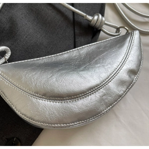 Detail of silver crescent bag featuring metallic leather texture and knotted strap design