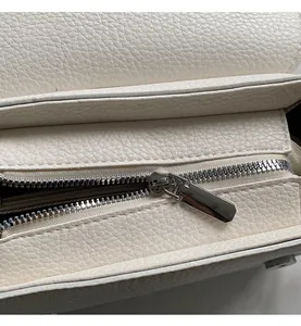 Close-up of smooth silver metal zipper and white lychee texture leather on the bag