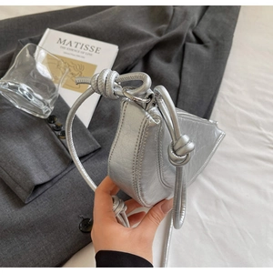 Detail view of silver crescent bag featuring knotted strap and metallic leather texture