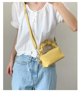 Detail of a bright yellow crossbody bag with a unique knot handle and silver charm