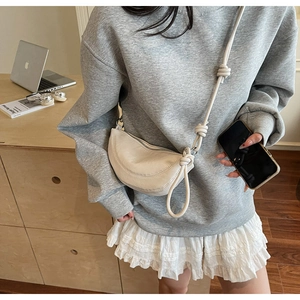Detail of off-white crescent crossbody bag with unique knotted strap and soft leather texture