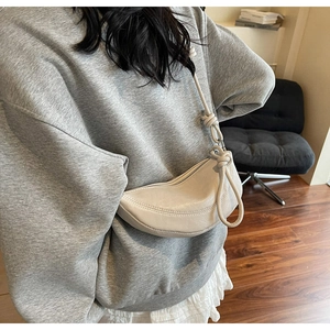 Detailed close-up of a beige crescent moon bag with stylish knot strap detail