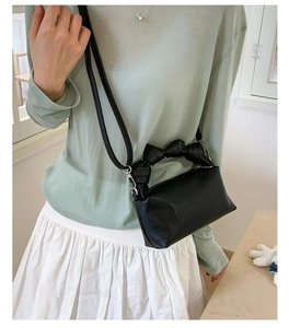 Detail of black lychee grain leather mini bag with a stylish top bow handle and strap