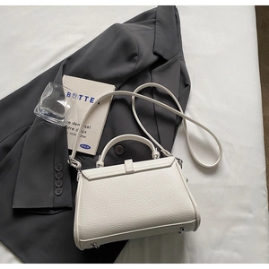 Detailed view of white litchi grain leather trapezoid bag with metal studs and strap