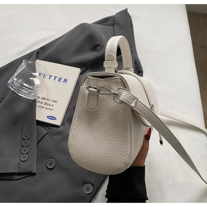 Detail of cream lychee leather texture and silver hardware on a chic crossbody bag