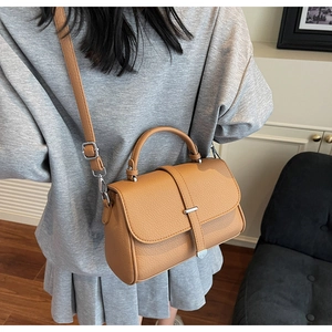 Detail of camel textured leather shoulder bag with top handle and metal buckle hardware