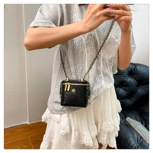 Detail of a mini black faux crocodile pattern box bag with a golden flower logo