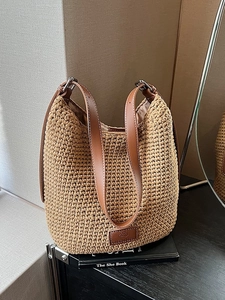 Woven straw bucket bag with dark brown leather straps on a minimalist background
