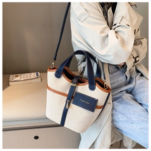 Dettaglio della borsa a secchiello in tela con finiture in pelle indossata con trench