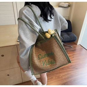 Detail of straw tote bag with green Summer Vibes embroidery and braided handles