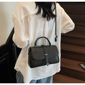 Detail of black lychee grain leather handbag with silver hardware on a model
