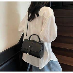 Model wearing black pebble leather crossbody bag with top handle and metal buckle detail