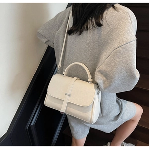 Detailed shot of white lychee leather texture and silver metal clasp on women's handbag