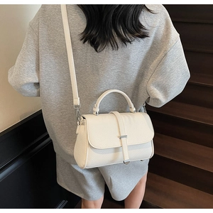 Detail of white lychee pattern crossbody bag with silver buckle worn by a model