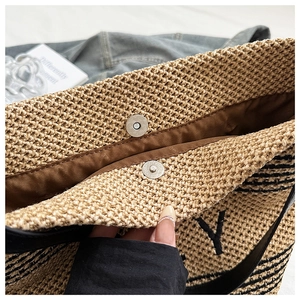 Detail of straw bucket bag with magnetic closure, silk lining, and embroidered letter