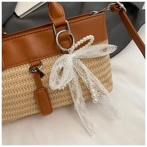 Close-up of straw woven tote with leather panel, lace bow and pearl charm detail