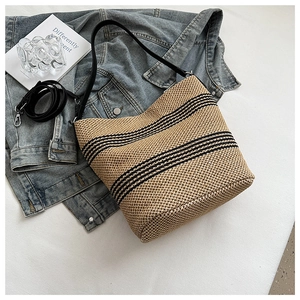 Detail of hand-woven straw bucket bag with black stripes and leather shoulder strap