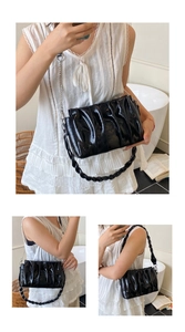 Detail of black pleated patent leather bag with thick handle and metal chain strap