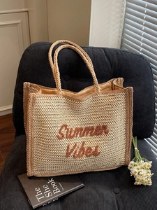 Summer Vibes straw woven tote bag with brown embroidery on a stylish black corduroy armchair