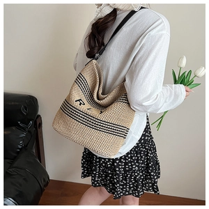 Detail shot of woven straw bucket bag with black stripes and R logo held by a model