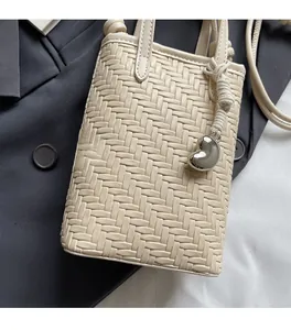 Close-up of cream woven mini crossbody bag with a silver heart charm and braided detail