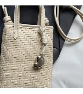 Detail of beige woven mini bag with white cotton rope handle and silver heart charm