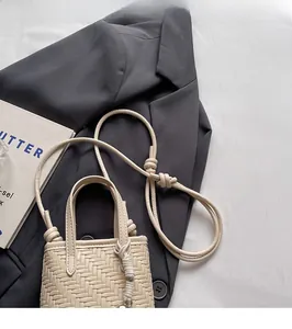 Detail of cream woven mini crossbody bag with adjustable knotted shoulder strap on blazer