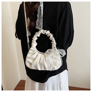 Détail du sac hobo crème avec texture plissée et breloque noeud en perles et dentelle
