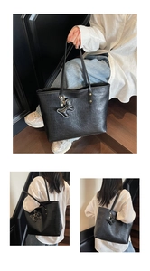 Detail of black crocodile texture tote bag with a matching bear charm and long straps
