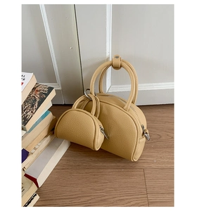 Détail d'un sac bowling en cuir grainé beige avec son petit pendentif sur sol en bois