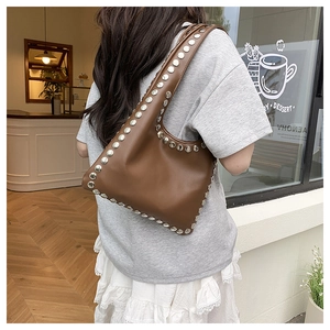 Détail d'un sac cabas en cuir marron avec deux rangées de grands rivets argentés sur le bord