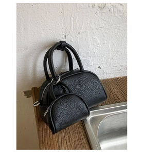 Détail du sac bowling noir à grain de litchi avec mini pochette sur une surface en bois