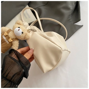 Detail of cream white pleated bucket bag with cute brown plush bear charm and thin strap